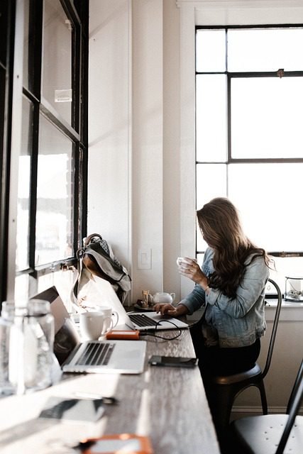 A woman working on a laptop to find the best flight deals while sitting on a tropical beach with palm trees and ocean views.