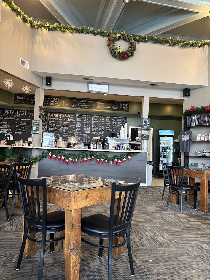 ozy interior of a local coffee shop decorated for Christmas with a lit evergreen tree, hanging garland, and warm festive fairy lights.