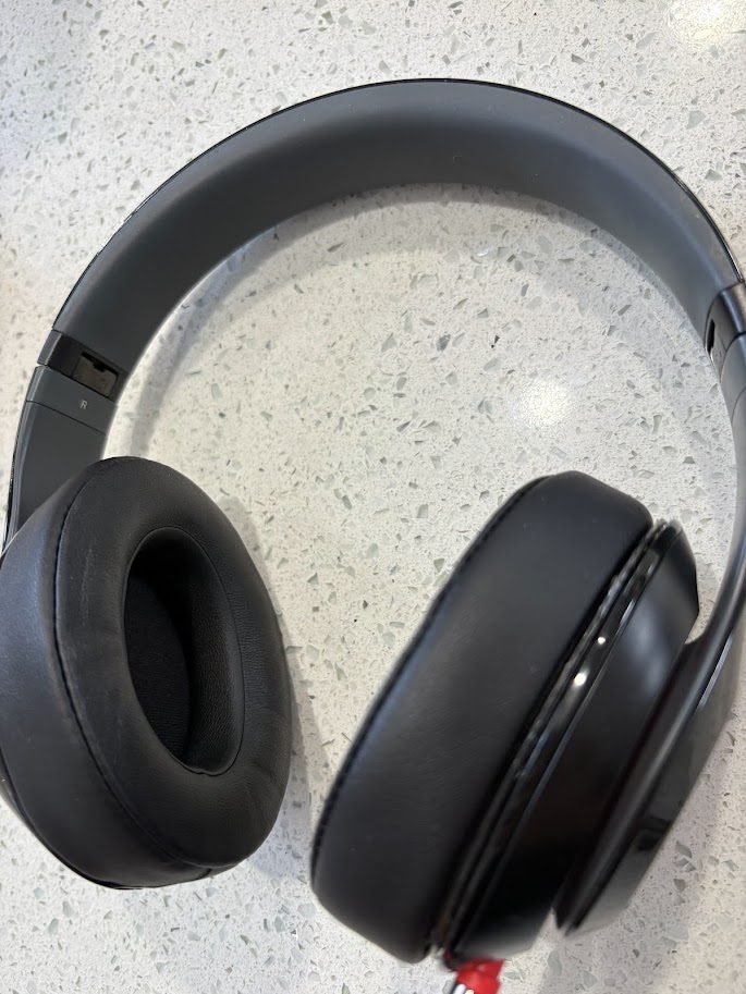 A pair of classic matte black Beats over-ear headphones with newly installed black ear cushions resting on a kitchen counter. New ear cushions to extend the life of beats.