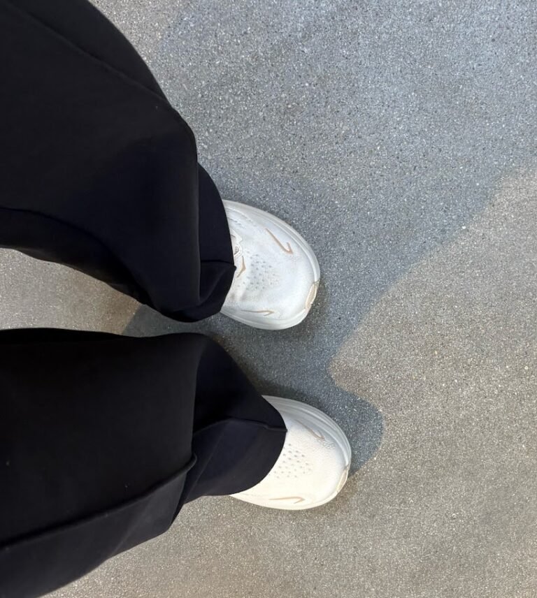Overhead view of white Hoka Clifton 10 sneakers being worn with black pants on concrete, emphasizing their comfort as the best travel shoes for carry-on travel.
