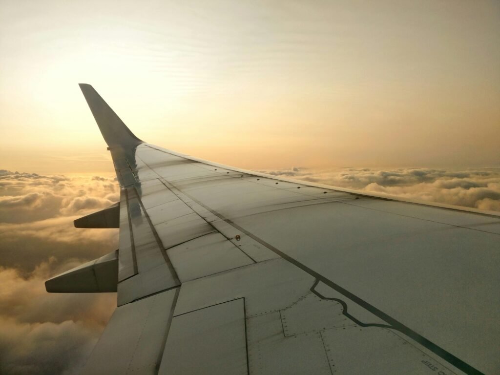 View of an airplane wing soaring above clouds during sunset, capturing flight serenity.