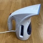 Back view of a blue and white compact travel steamer (HiLIFE brand) on a wooden floor, showing the large 240ml water tank.