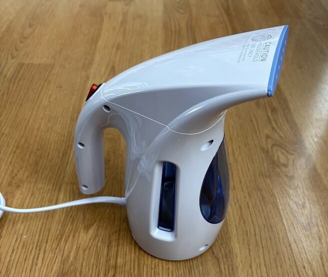 Back view of a blue and white compact travel steamer (HiLIFE brand) on a wooden floor, showing the large 240ml water tank.