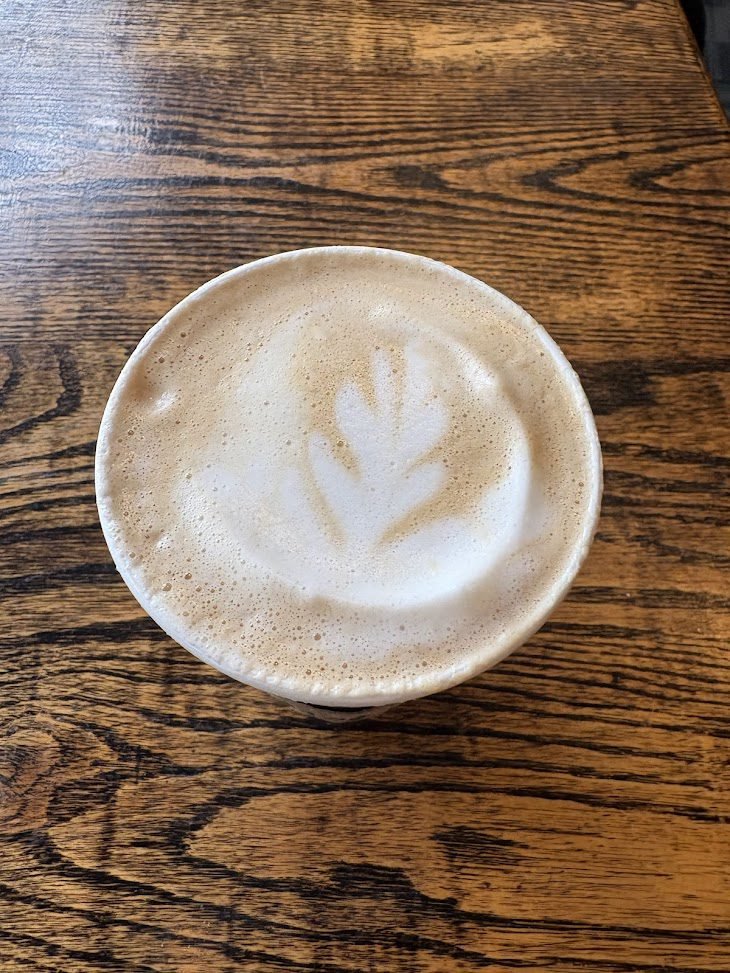 A top-down view of a specialty latte with leaf-pattern latte art in a white ceramic mug, set on a rustic dark wood table at Beans-n-Cream in Cedarville, Ohio.