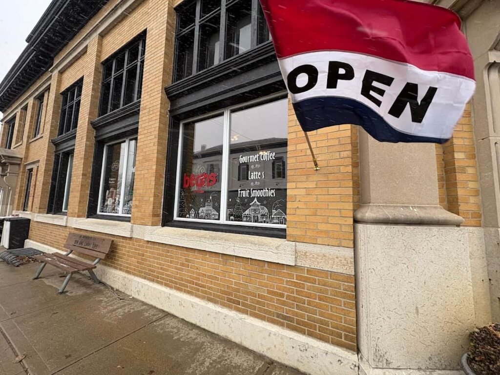 The brick exterior of Beans-n-Cream in Cedarville, Ohio, a relaxing coffee shop with a red, white, and blue "OPEN" flag and window art. A Relaxing coffee shop.