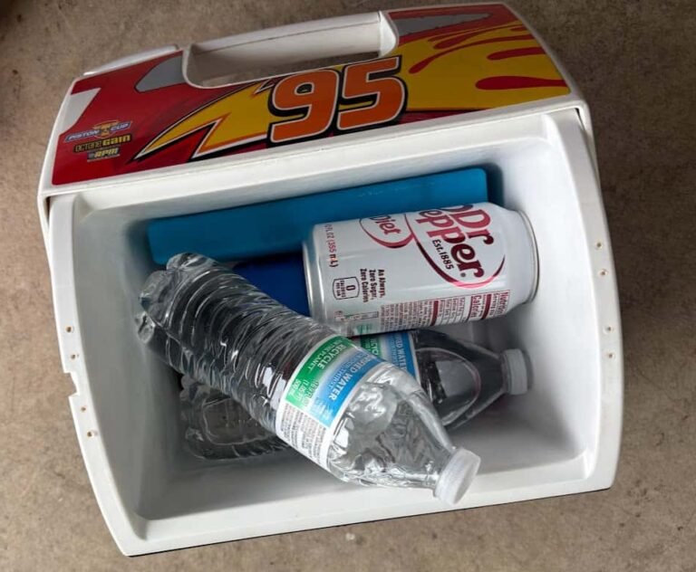 An overhead view of a small white personal cooler containing a Diet Dr Pepper can, two water bottles, and a blue ice pack.