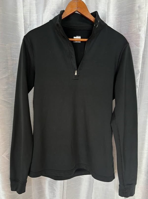 A black long-sleeve quarter-zip athletic pullover hanging on a wooden hanger, functioning as a wicking base layer for winter hiking.