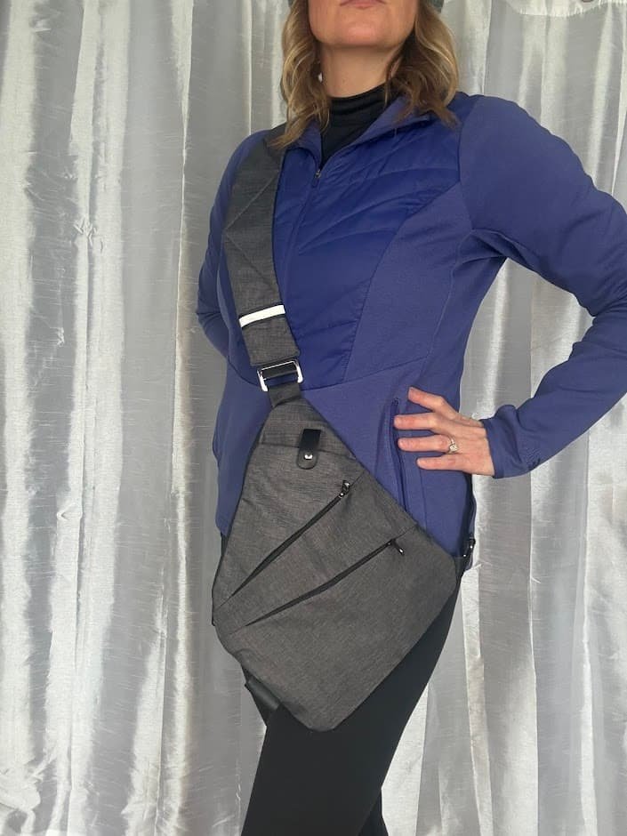 A woman wearing the best anti theft crossbody bag for travel in charcoal gray over a purple jacket, demonstrating its slim, ergonomic, and secure fit.