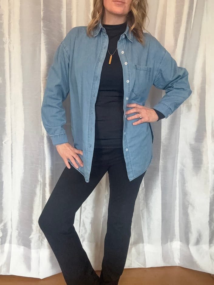 A woman modeling the best denim button down for travel worn open as a light layer over a black turtleneck and black pants.