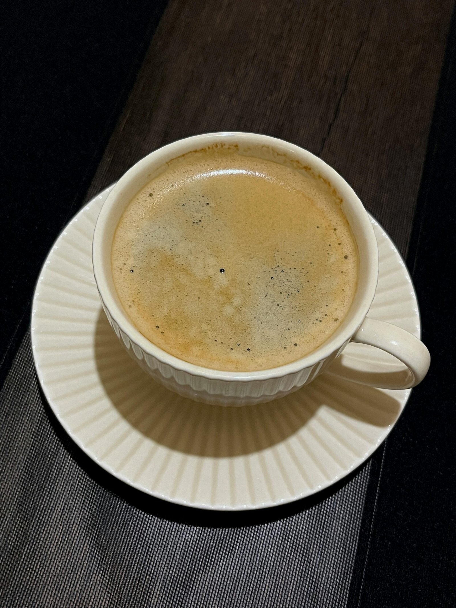 Top view of a hot cup of coffee with foam on a wooden table.