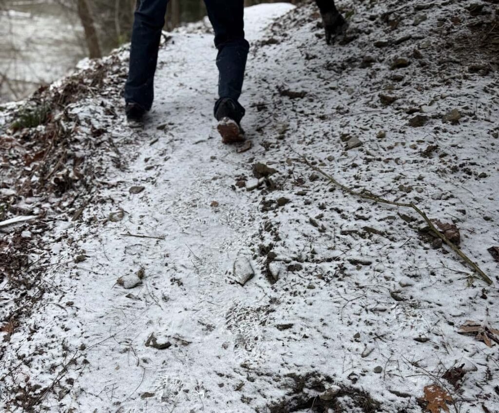 A close-up of a hiker's boots navigating a steep, icy trail covered in light snow at Mohican State Park.
