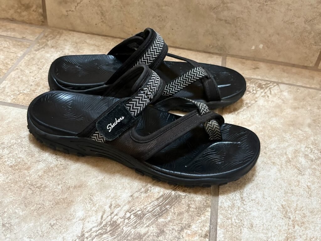 A pair of black Skechers Women's Reggae Trailway flip-flop sandals, shown to have a durable sole and comfortable straps, representing the best women travel sandals for walking.