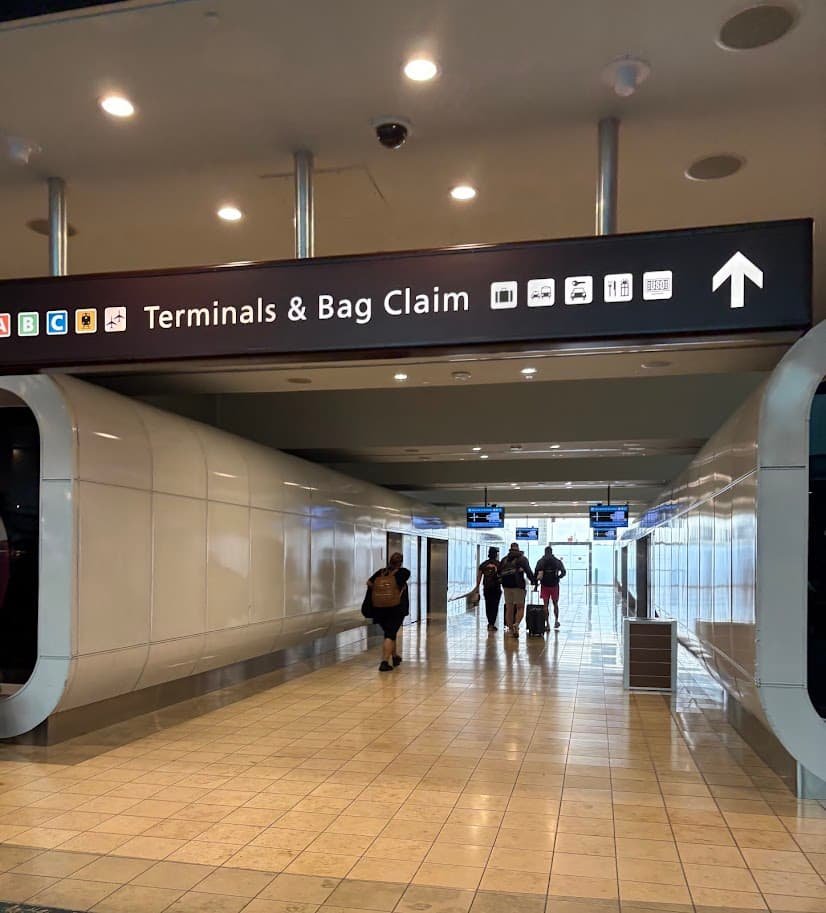Directional signage at Orlando International Airport (MCO) showing arrows for Terminals A, B, and C and baggage claim above an automated people mover (APM) station.