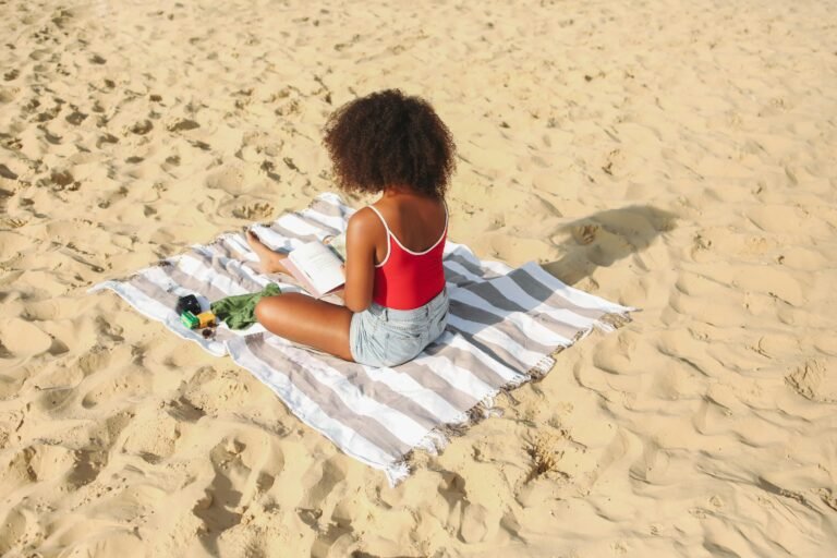 A woman enjoying leisure time reading on a sandy beach, creating a serene summer vibe.