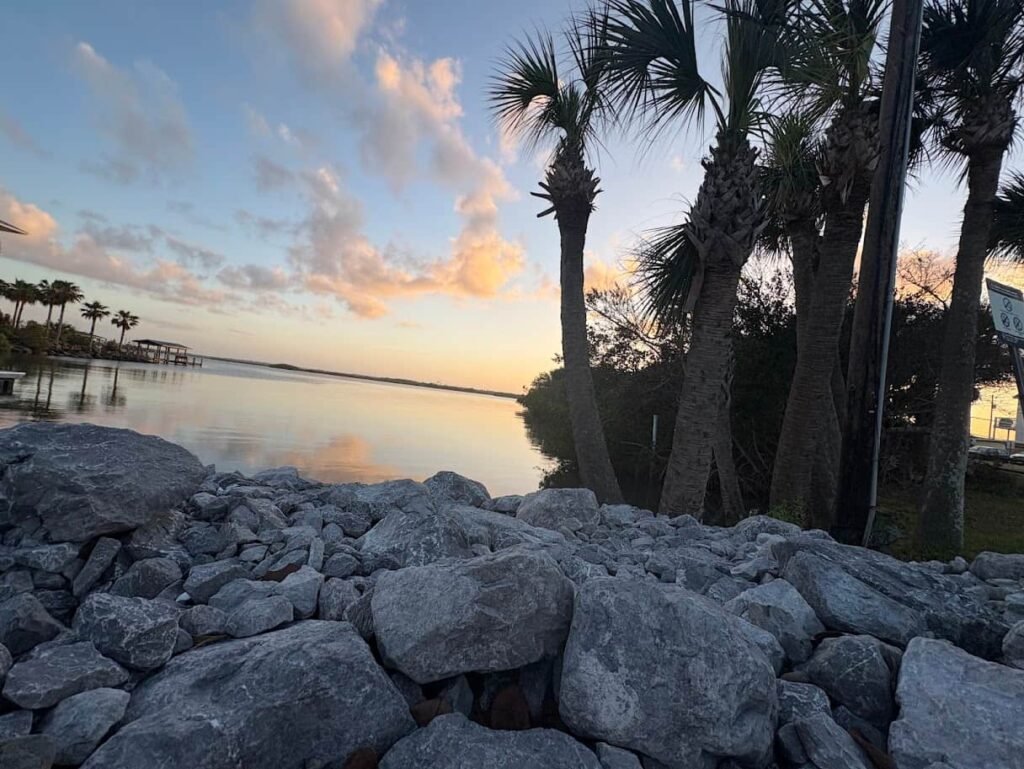 A wide-angle view of a golden sunrise over the Atlantic Ocean at New Smyrna Beach, with gentle waves crashing on a sandy shore and long sunbeams reflecting on the wet sand.