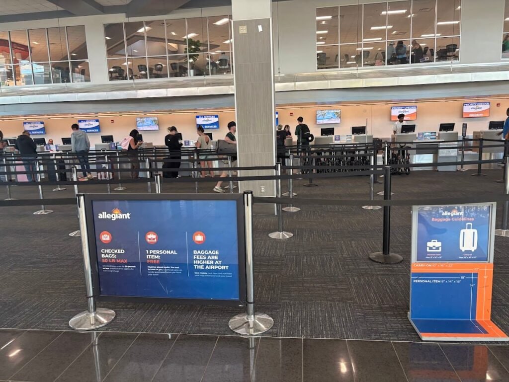 The Allegiant Air check-in area at Orlando Sanford International Airport (SFB) featuring blue baggage guideline signs for checked bags, free personal items, and carry-ons in front of a row of service counters.