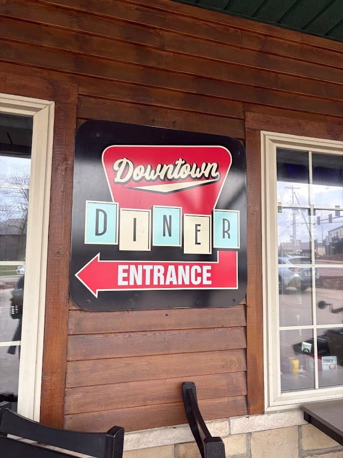 A retro-style sign for the Downtown Diner in Berlin, Ohio. The sign features a red heart shape at the top with "Downtown" in script, blue-and-white tiles spelling out "DINER," and a red arrow pointing toward the entrance on a rustic wooden wall.