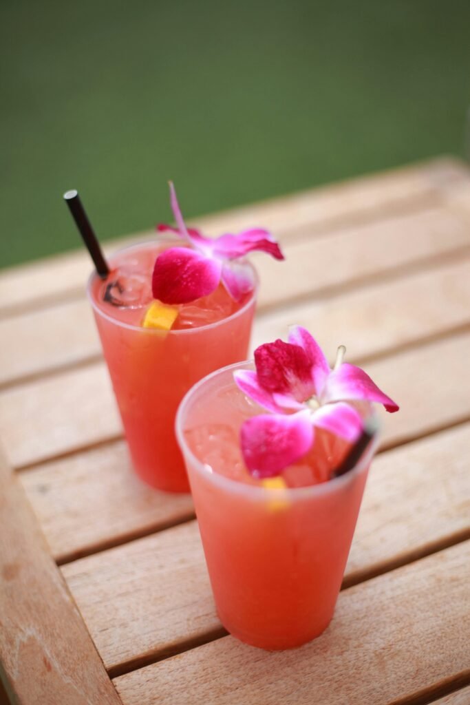 Two vibrant cocktails with orchid garnish on a wooden table, perfect for refreshing summer days.