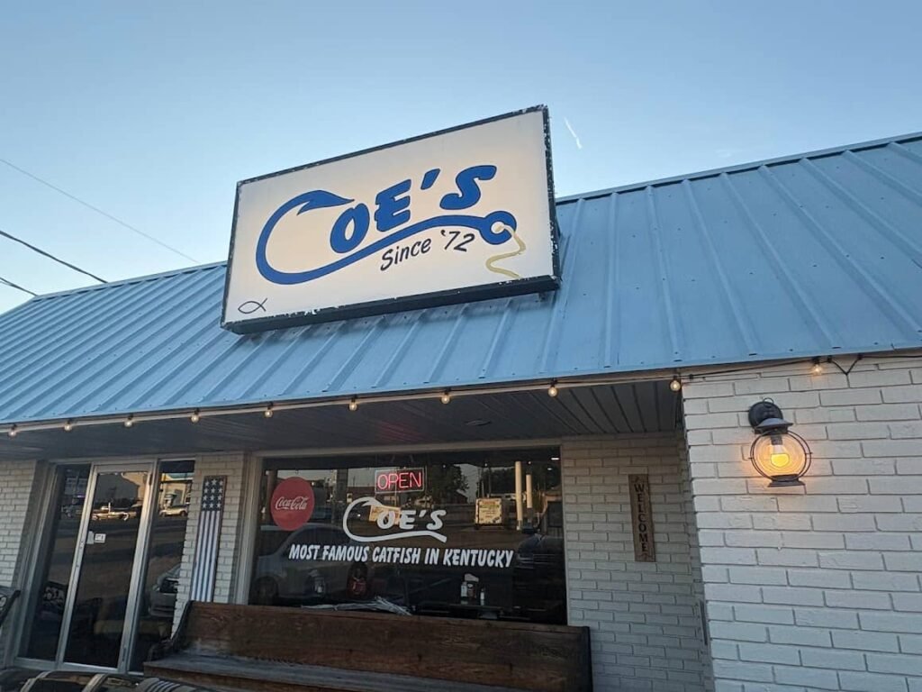 The exterior storefront of Coe's Restaurant in Russell Springs, Kentucky, featuring a blue metal roof and a large sign that reads "Coe's Since '72" alongside a window stating "Most Famous Catfish in Kentucky."