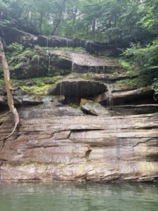 Water trickling down a tall, layered rock shelf waterfall surrounded by green trees into the lake during a lake vacation.