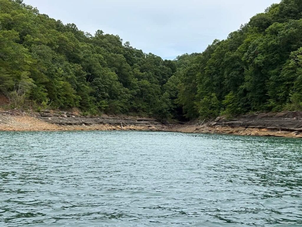 A quiet, secluded water cove surrounded by steep, densely forested hills and exposed rocky shorelines during a lake vacation at Lake Cumberland.