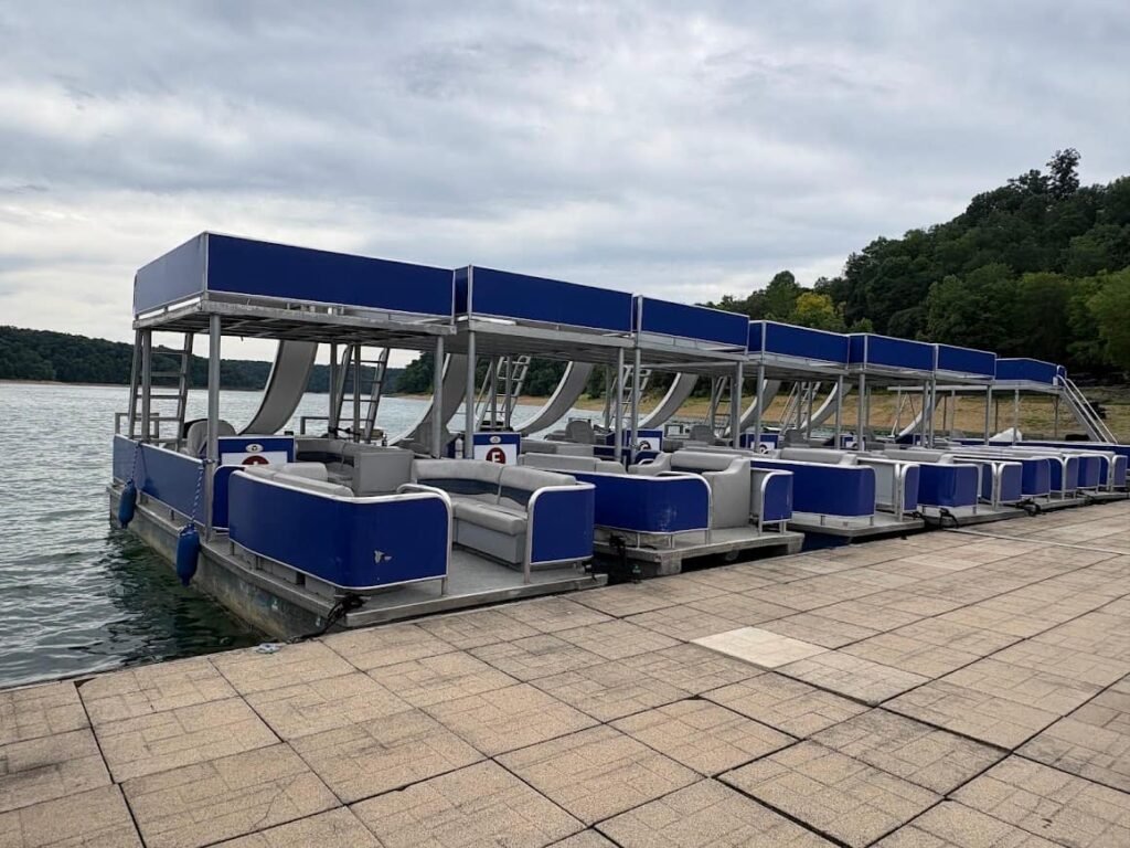 A row of blue and silver double-decker pontoon boats with water slides docked at a Lake Cumberland marina during a family lake vacation.