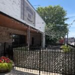 The exterior patio and storefront of Charred Oak Grill in downtown Somerset, Kentucky, featuring a brick building, a black metal fence, and outdoor string lights under a bright blue sky.