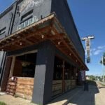 The dark-painted exterior of The Makers Mill artisan shop in downtown Somerset, Kentucky, featuring a rustic wooden and corrugated metal awning, string lights, and a vintage guitar-shaped sign that reads "Live Music."