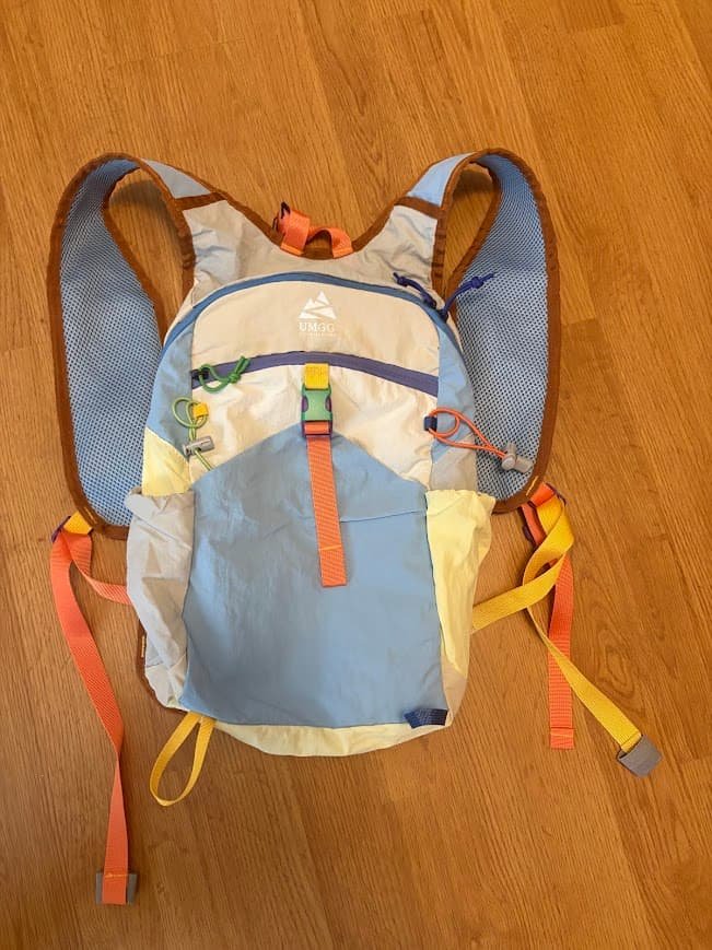 A colorful 15L packable hiking daypack with light blue, yellow, and orange straps resting flat on a light wood floor.