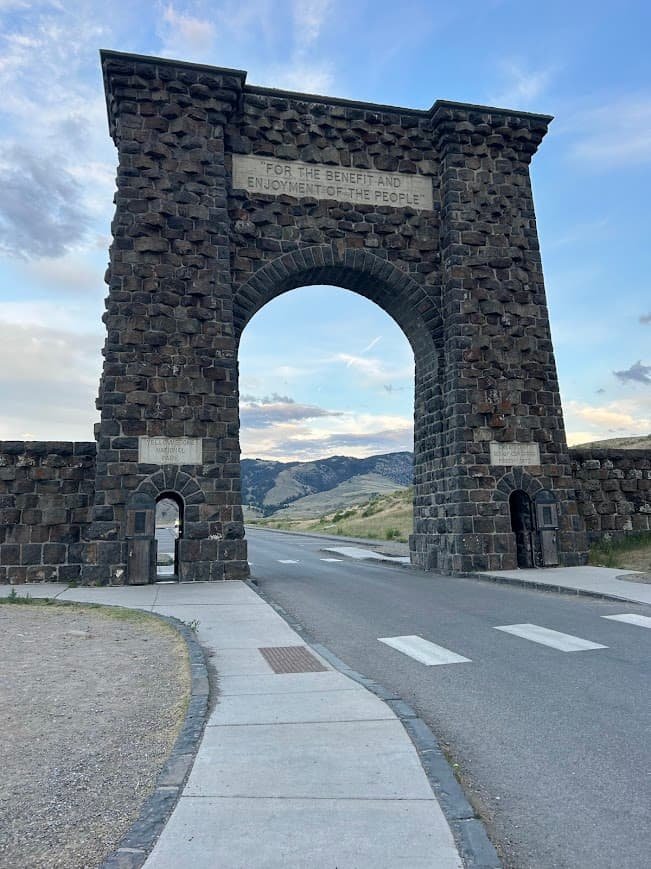 Gardiner Montana north entrance Yellowstone Roosevelt Arch with mountains in the background during summer. Plan a Yellowstone Trip from Gardiner