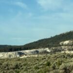 Here is the complete, SEO-optimized image metadata package for this beautiful landscape photo. This shot beautifully captures the cascading travertine mineral structures of Mammoth Hot Springs rising out of the brush. It is a perfect fit for your Day 3 itinerary section, perfectly illustrating just how quickly you hit these mind-blowing geothermal features after driving through the park gate. Image Metadata Package File Name Idea: mammoth-hot-springs-gardiner-montana-yellowstone-itinerary.jpg Alt Text: Mammoth Hot Springs Gardiner Montana mineral terraces inside Yellowstone National Park on a clear summer day.