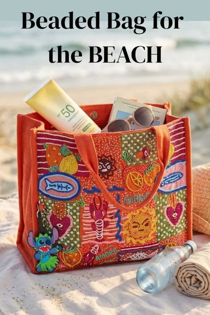 A colorful hand-beaded orange tote bag sitting on a sandy beach blanket, packed with beach essentials including SPF 50 sunscreen, sunglasses, a book, a rolled towel, and a water bottle, with soft ocean waves blurred in the background.