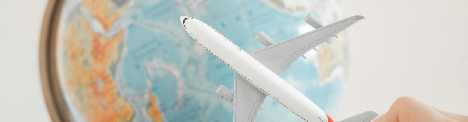 Close-up of a hand with a toy airplane in front of a globe, symbolizing travel and exploration.